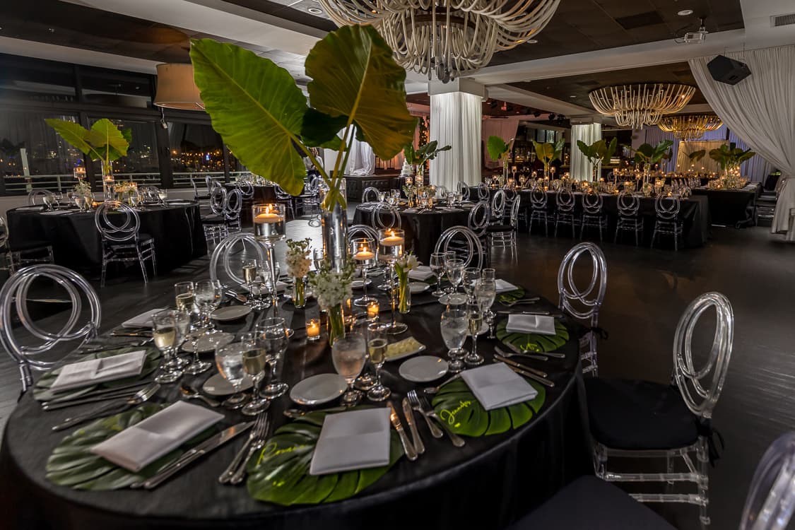 Reception tables in black linen with monstera leaves and the Miami skyline beyond